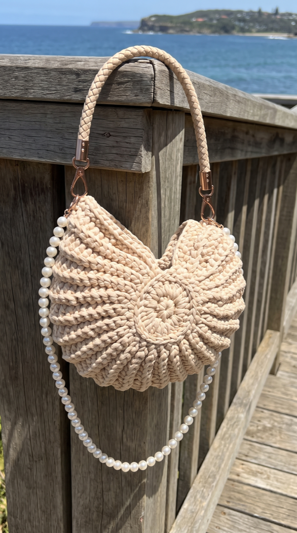 Shell handbag on a sunny deck railing above the water
