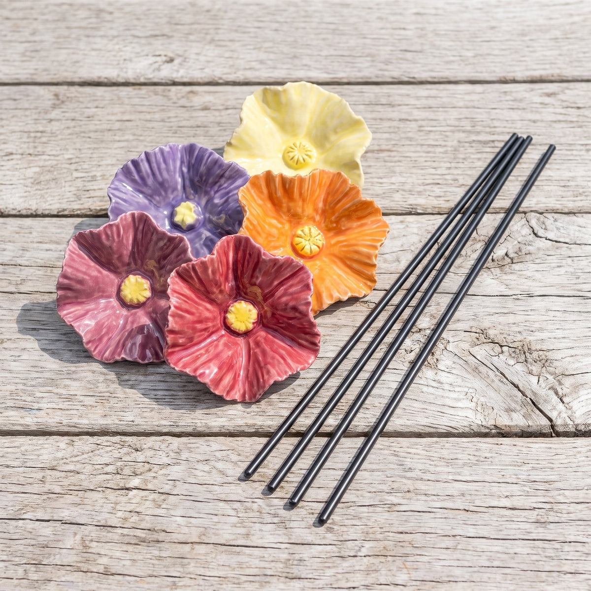 The set of four ceramic bee bowls laid out on weathered timber with their steel stakes