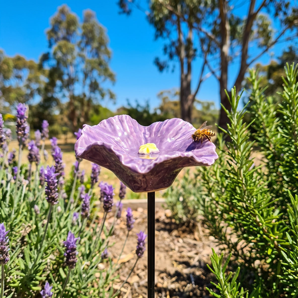 Purple ceramic bee bowl on its stake among flowering lavender, low angle against blue sky