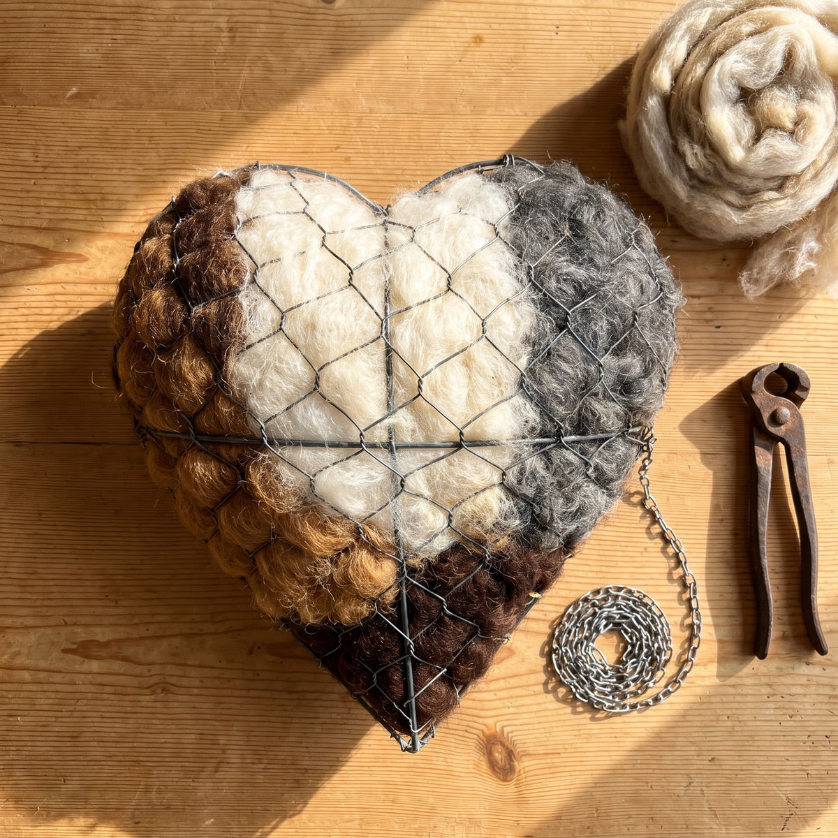 The nesting heart on a pine table with its hanging chain and fencing pliers