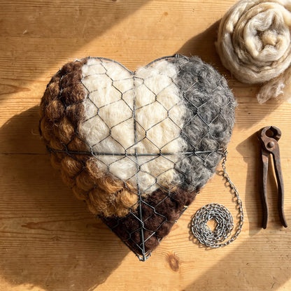 The nesting heart on a pine table with its hanging chain and fencing pliers